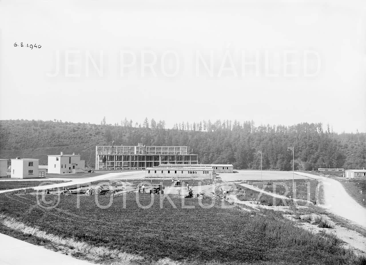 Příprava stavby společenského domu: v pozadí tovární budovy, dřevěné ubikace a vila vedoucího závodu na fotografii z 6. 8. 1940 (Photoclub Zruč nad Sázavou).